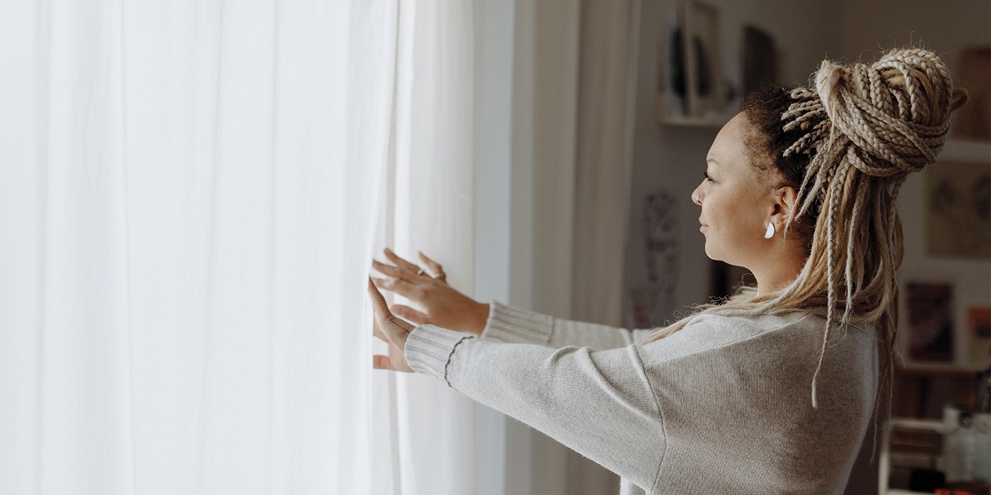 Woman opening curtains of window to let sunlight into the room