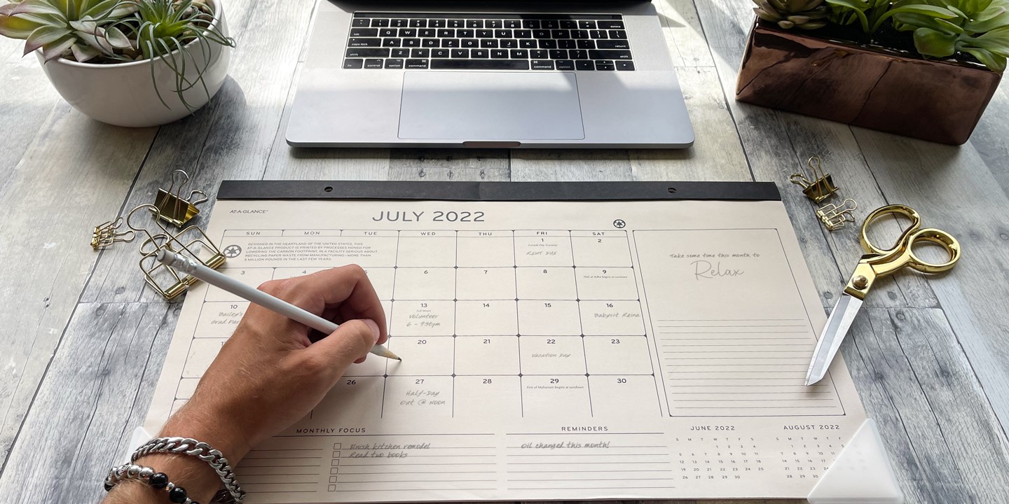 Deskpad calendar showing July 2022 with person writing on it
